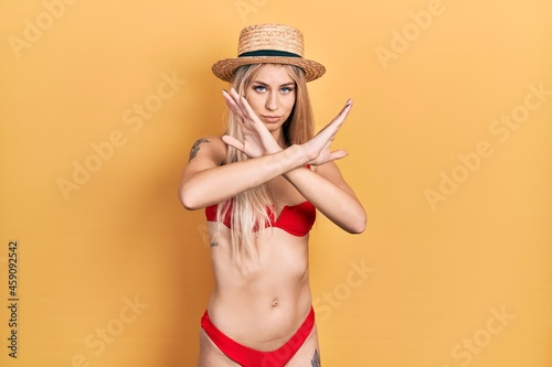 Young caucasian woman wearing bikini and summer hat rejection expression crossing arms doing negative sign, angry face