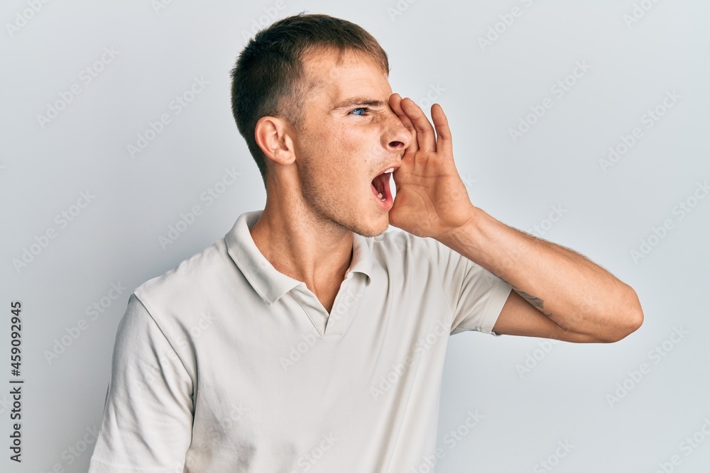 Young caucasian man wearing casual white polo shouting and screaming loud to side with hand on mouth. communication concept. Young caucasian man wearing casual white polo shouting and screaming loud to side with hand on mouth. communication concept.