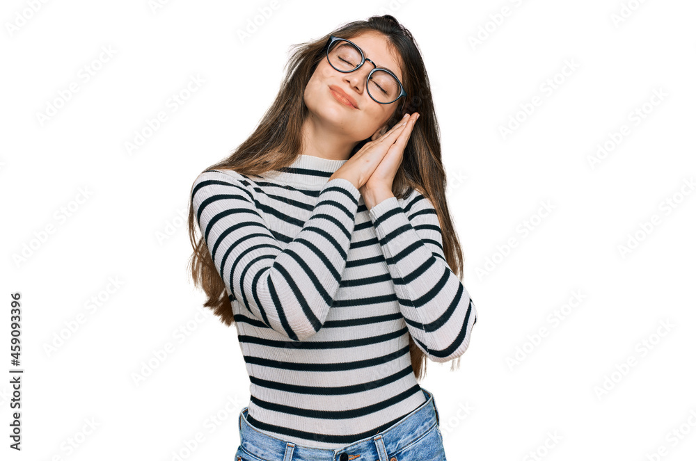 Young beautiful teen girl wearing casual clothes and glasses sleeping tired dreaming and posing with hands together while smiling with closed eyes. Young beautiful teen girl wearing casual clothes and glasses sleeping tired dreaming and posing with hands together while smiling with closed eyes.