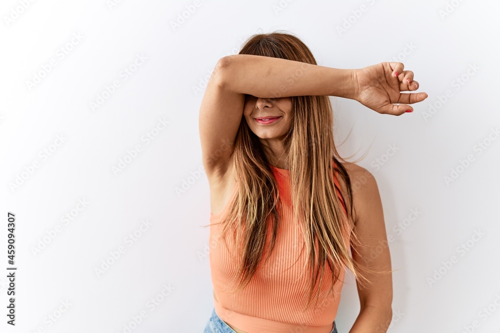 Hispanic woman with bang hairstyle standing over isolated background covering eyes with arm smiling cheerful and funny. blind concept. Hispanic woman with bang hairstyle standing over isolated background covering eyes with arm smiling cheerful and funny. blind concept.