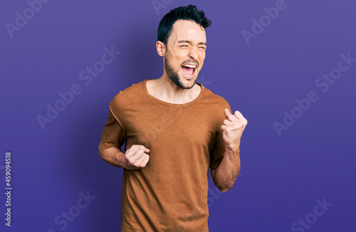 Hispanic man with beard wearing casual t shirt celebrating surprised and amazed for success with arms raised and eyes closed