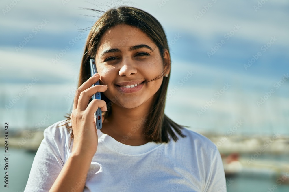 Young latin girl smiling happy talking on the smartphone at the beach