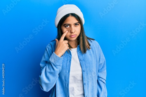 Young latin woman wearing cute wool cap pointing to the eye watching you gesture, suspicious expression © Krakenimages.com