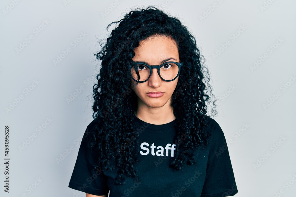 Young hispanic woman with curly hair wearing staff t shirt skeptic and nervous, frowning upset because of problem. negative person. Young hispanic woman with curly hair wearing staff t shirt skeptic and nervous, frowning upset because of problem. negative person.