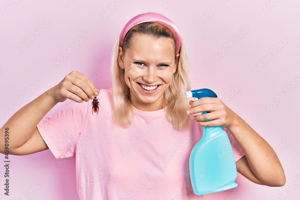 Beautiful caucasian blonde woman holding cockroach and pesticide sprayer smiling and laughing hard out loud because funny crazy joke. Beautiful caucasian blonde woman holding cockroach and pesticide sprayer smiling and laughing hard out loud because funny crazy joke.