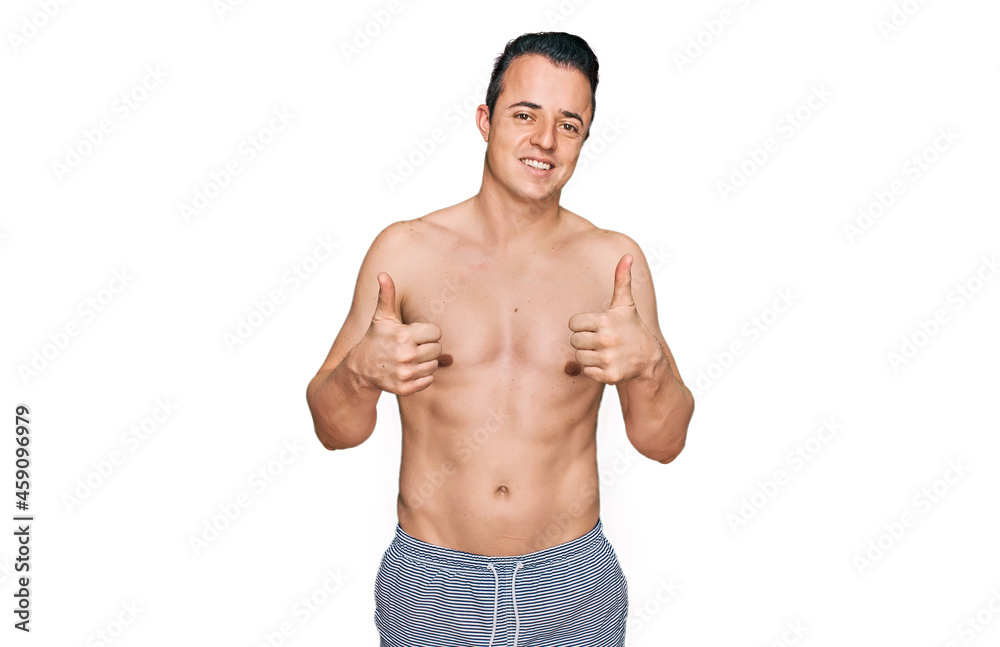 Handsome young man wearing swimwear shirtless success sign doing positive gesture with hand, thumbs up smiling and happy. cheerful expression and winner gesture. Handsome young man wearing swimwear shirtless success sign doing positive gesture with hand, thumbs up smiling and happy. cheerful expression and winner gesture.