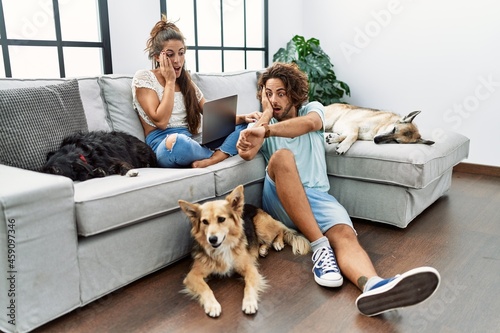 Young hispanic couple with dogs relaxing at home looking at the watch time worried, afraid of getting late