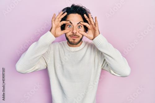 Handsome hispanic man wearing casual white sweater trying to open eyes with fingers, sleepy and tired for morning fatigue © Krakenimages.com
