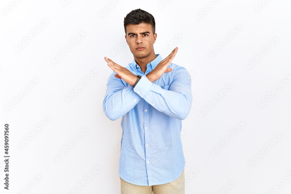 Young hispanic man wearing business shirt standing over isolated background rejection expression crossing arms doing negative sign, angry face Young hispanic man wearing business shirt standing over isolated background rejection expression crossing arms doing negative sign, angry face