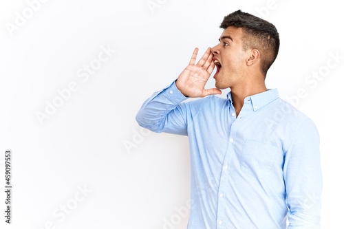 Young hispanic man wearing business shirt standing over isolated background shouting and screaming loud to side with hand on mouth. communication concept. © Krakenimages.com