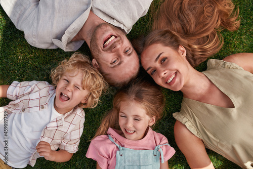 Top view of happy young parents with little daughter and son lying on green grass in summer park