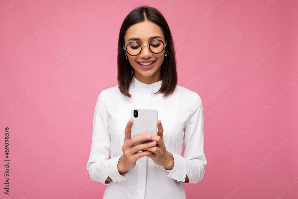 Photo shot of attractive positive good looking young woman wearing casual stylish outfit poising isolated on background with empty space holding in hand and using mobile phone messaging sms looking at Photo shot of attractive positive good looking young woman wearing casual stylish outfit poising isolated on background with empty space holding in hand and using mobile phone messaging sms looking at