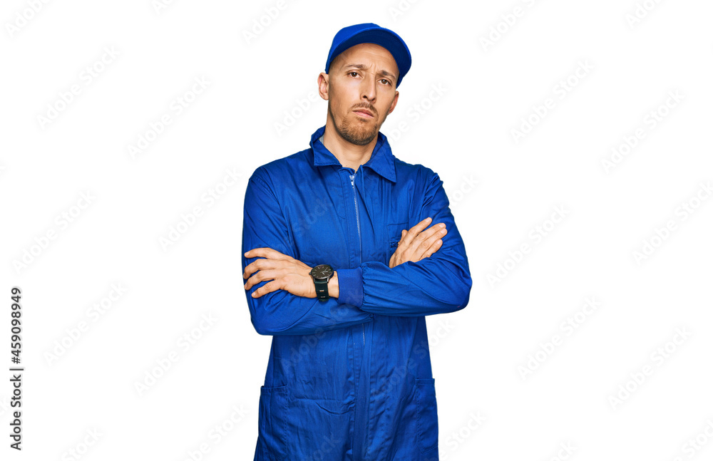 Bald man with beard wearing builder jumpsuit uniform skeptic and nervous, disapproving expression on face with crossed arms. negative person. Bald man with beard wearing builder jumpsuit uniform skeptic and nervous, disapproving expression on face with crossed arms. negative person.
