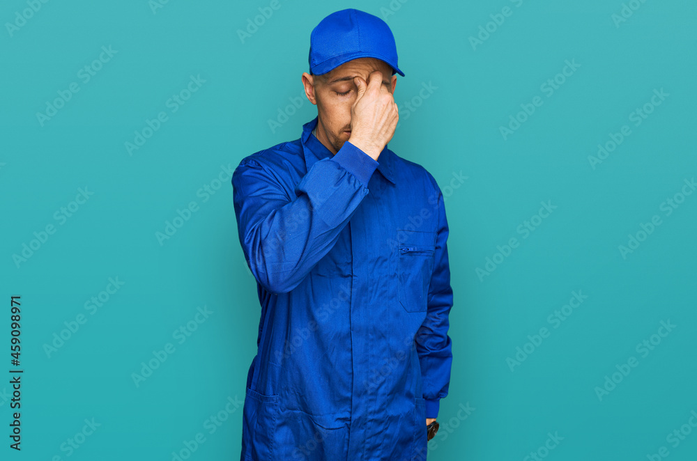 Bald man with beard wearing builder jumpsuit uniform tired rubbing nose and eyes feeling fatigue and headache. stress and frustration concept.