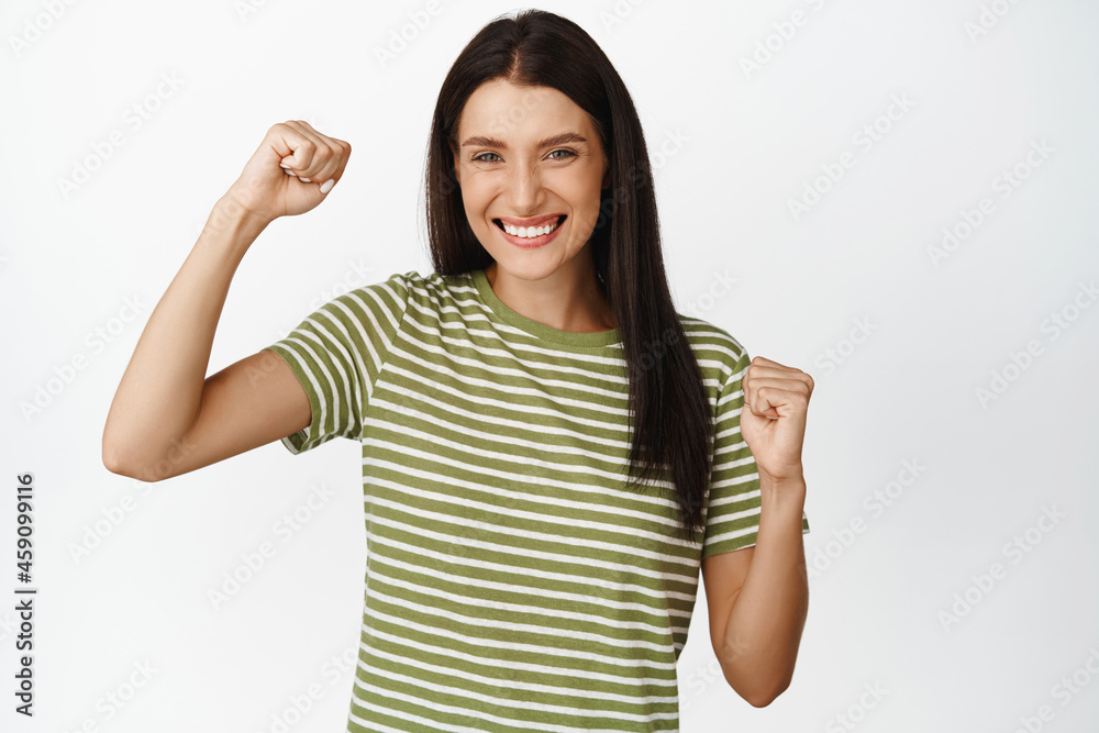 Yes. Excited brunette woman winning, celebrating and jumping with fist pumps, smiling pleased, standing happy against white background Yes. Excited brunette woman winning, celebrating and jumping with fist pumps, smiling pleased, standing happy against white background