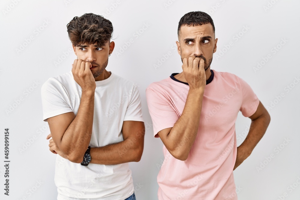 Young gay couple standing over isolated background looking stressed and nervous with hands on mouth biting nails. anxiety problem. Young gay couple standing over isolated background looking stressed and nervous with hands on mouth biting nails. anxiety problem.