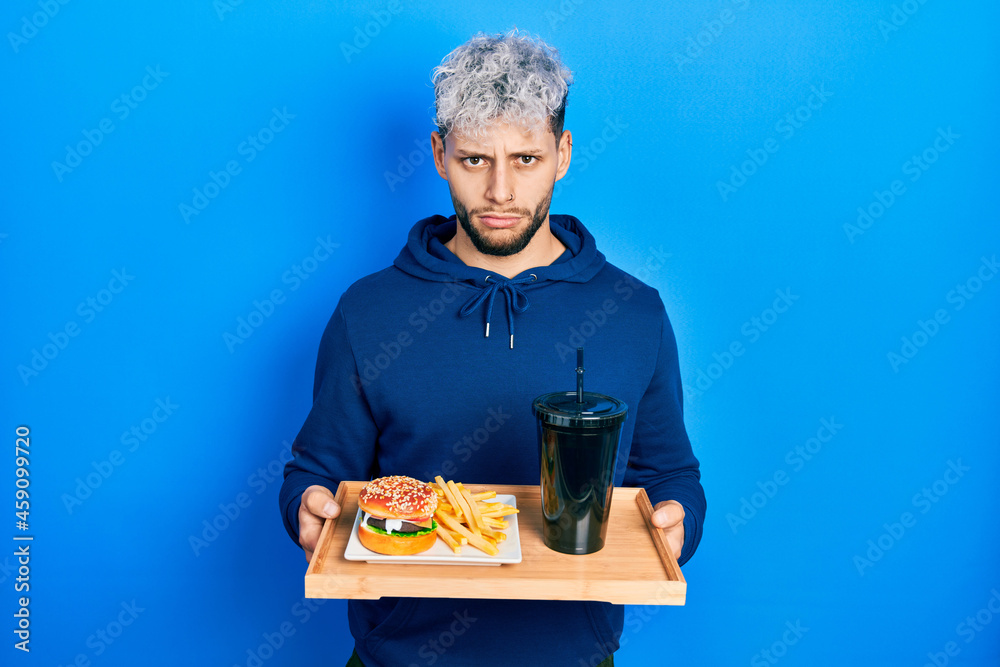 Young hispanic man with modern dyed hair eating a tasty classic burger with fries and soda depressed and worry for distress, crying angry and afraid. sad expression. Young hispanic man with modern dyed hair eating a tasty classic burger with fries and soda depressed and worry for distress, crying angry and afraid. sad expression.