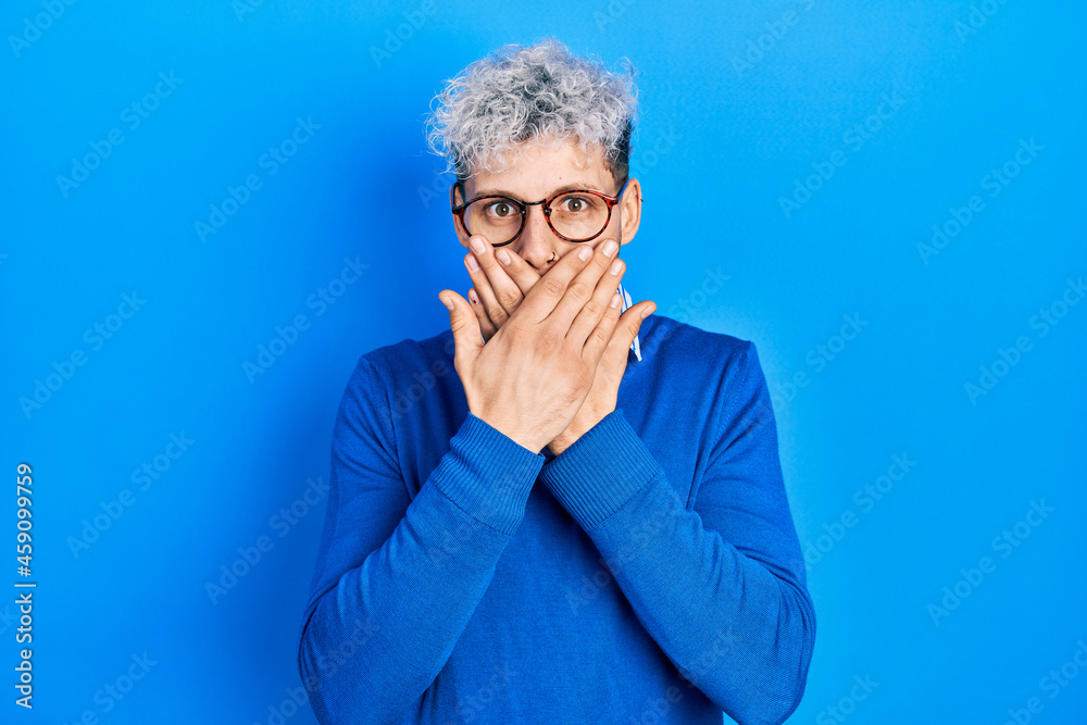 Young hispanic man with modern dyed hair wearing sweater and glasses shocked covering mouth with hands for mistake. secret concept. Young hispanic man with modern dyed hair wearing sweater and glasses shocked covering mouth with hands for mistake. secret concept.