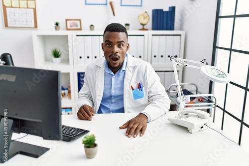 Young african doctor man wearing stethoscope at the clinic scared and amazed with open mouth for surprise, disbelief face