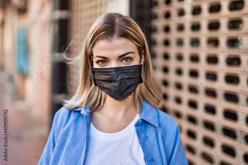 Young blonde girl wearing coronavirus protective mask standing at the city.