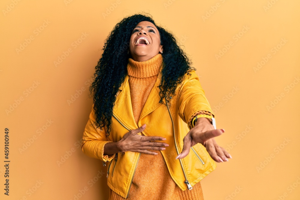 Middle age african american woman wearing wool winter sweater and leather jacket laughing at you, pointing finger to the camera with hand over body, shame expression