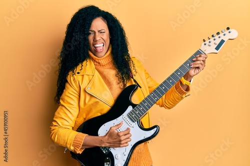 Middle age african american woman playing electric guitar winking looking at the camera with sexy expression, cheerful and happy face.