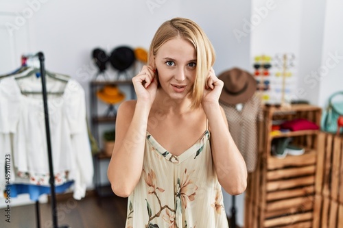 Young caucasian woman at retail shop covering ears with fingers with annoyed expression for the noise of loud music. deaf concept.