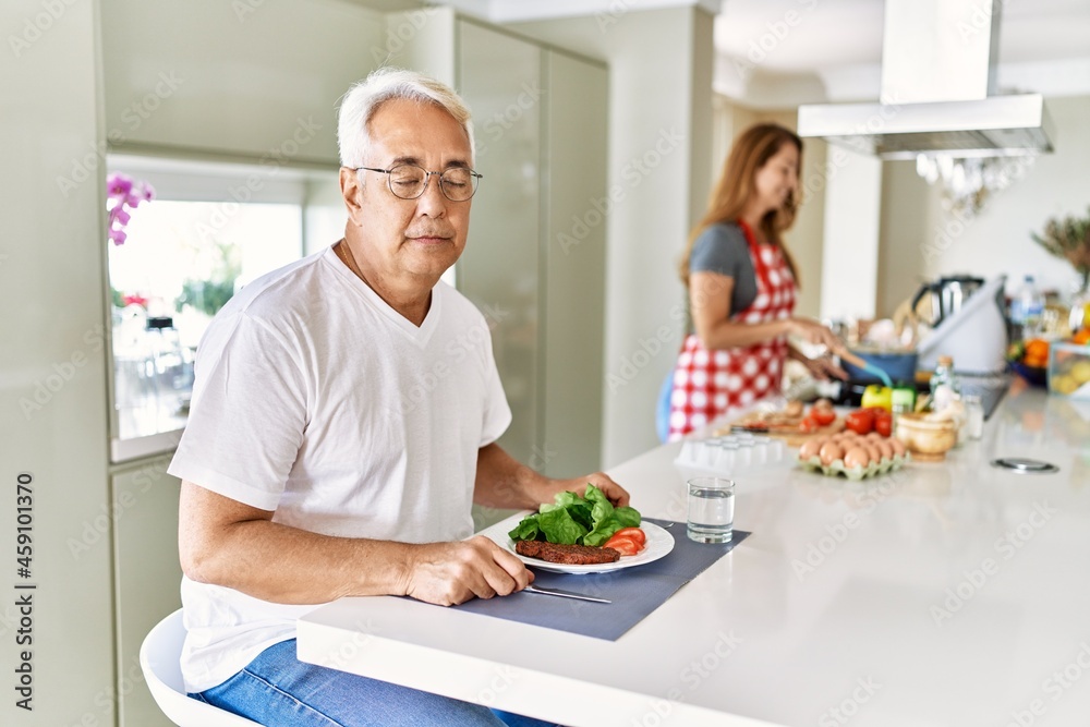 Middle age hispanic couple eating healthy meal at home thinking attitude and sober expression looking self confident