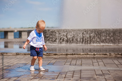 Toddler boy running through puddles close-up and copy space. Baby in embroidered shirt plays with water, Ukraine, Dnipro...