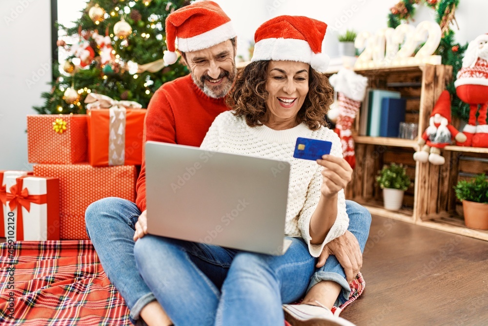 Middle age hispanic couple wearing christmas hat. Sitting on the floor using laptop and credit card at home. Middle age hispanic couple wearing christmas hat. Sitting on the floor using laptop and credit card at home.