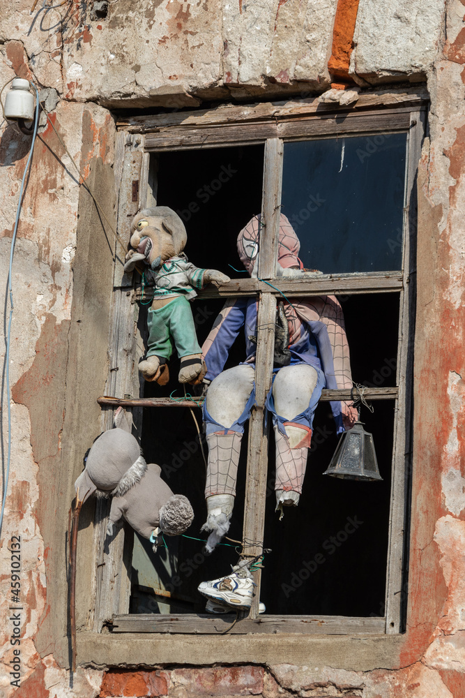 a strange old torn dolls in a wooden window in the orange wall of an old abandoned house