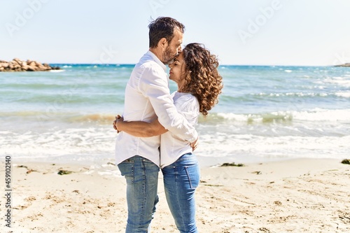 Middle age hispanic couple kissing and hugging standing at the beach.