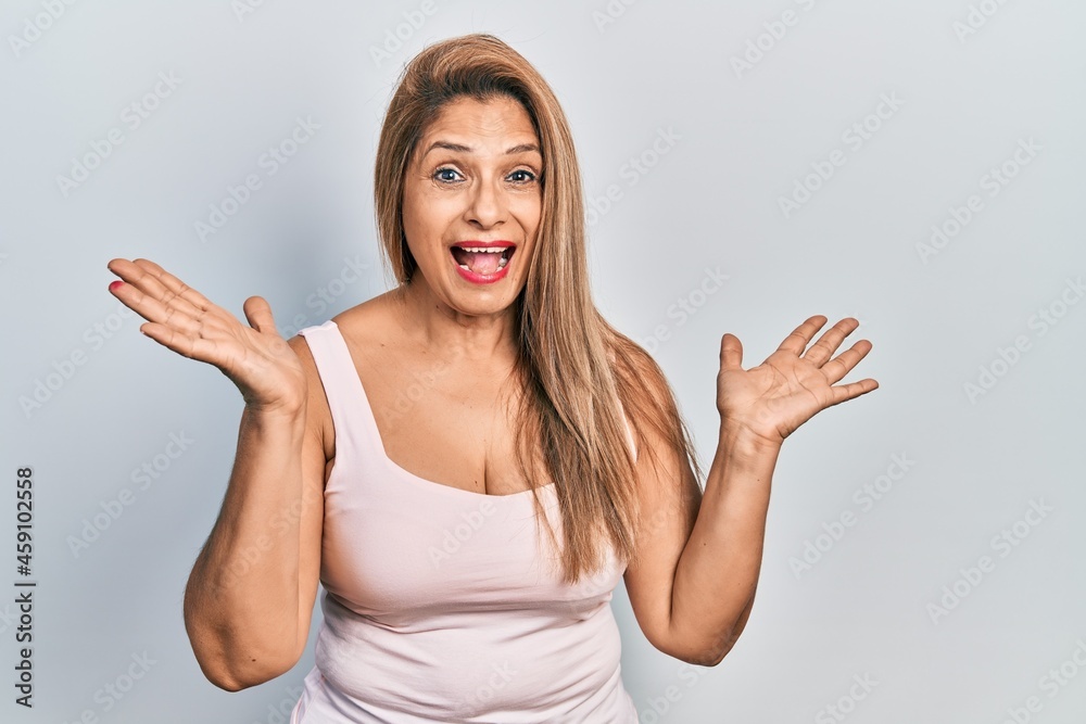 Middle age hispanic woman wearing casual style with sleeveless shirt celebrating crazy and amazed for success with arms raised and open eyes screaming excited. winner concept Middle age hispanic woman wearing casual style with sleeveless shirt celebrating crazy and amazed for success with arms raised and open eyes screaming excited. winner concept