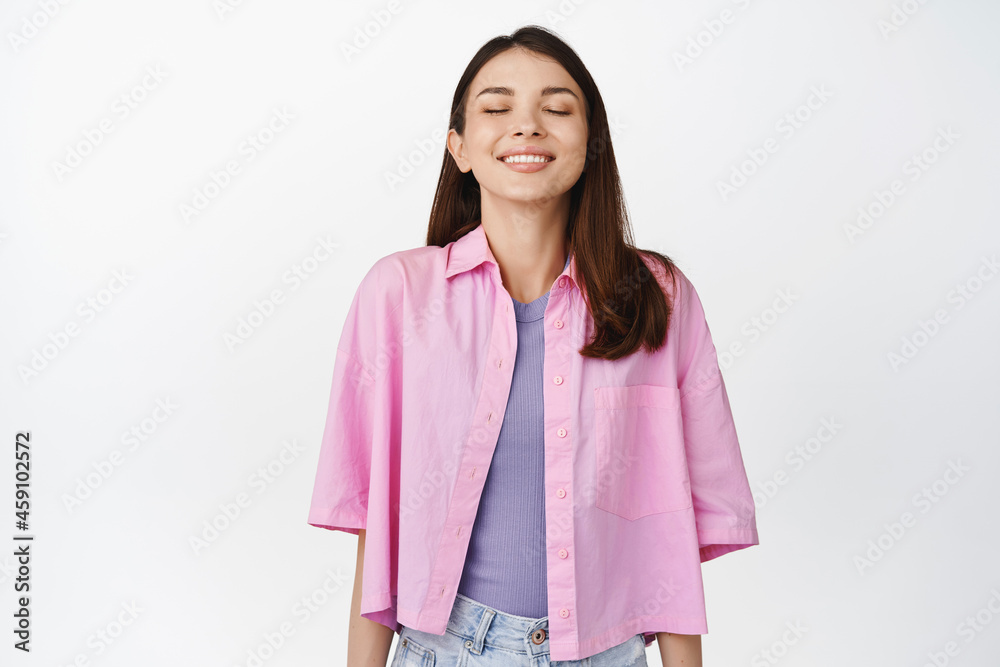 Smiling hopeful girl close her eyes, dreaming of something, making wish, standing against white background with uplifted face expression Smiling hopeful girl close her eyes, dreaming of something, making wish, standing against white background with uplifted face expression