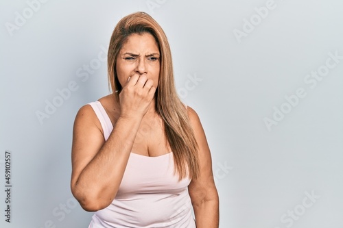 Middle age hispanic woman wearing casual style with sleeveless shirt looking stressed and nervous with hands on mouth biting nails. anxiety problem.