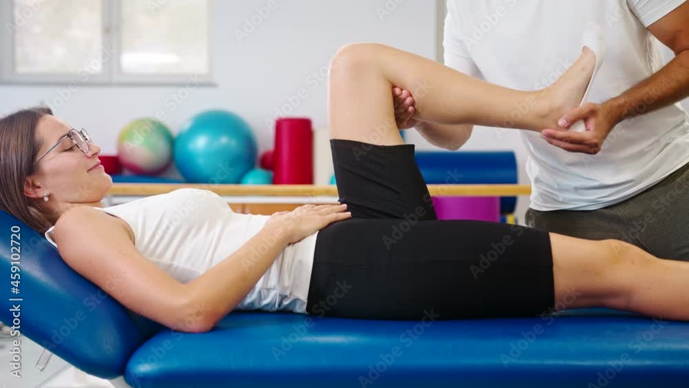 Handheld shot of a male Caucasian physiotherapist doing knee extension exercises with the female patient lying on the table