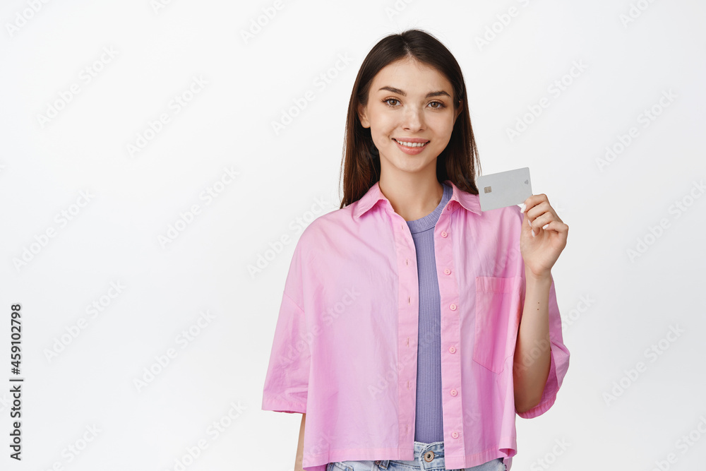 Young smiling woman showing her credit discount card, recommending bank or sale in store, standing over white background Young smiling woman showing her credit discount card, recommending bank or sale in store, standing over white background
