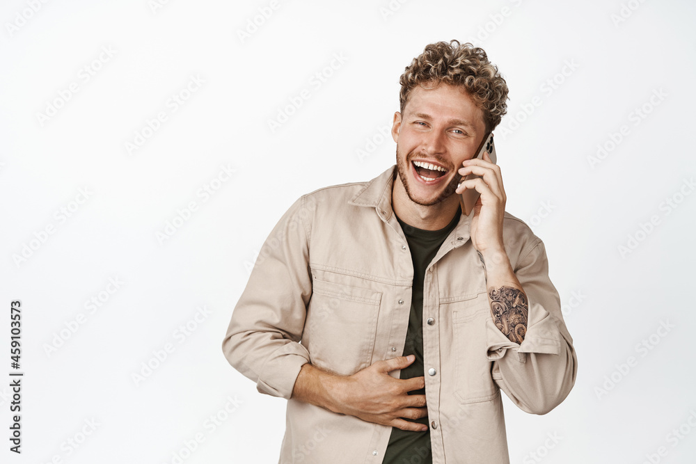Happy handsome guy laughing on phone, talking on cellphone and chuckle carefree, standing over white background Happy handsome guy laughing on phone, talking on cellphone and chuckle carefree, standing over white background