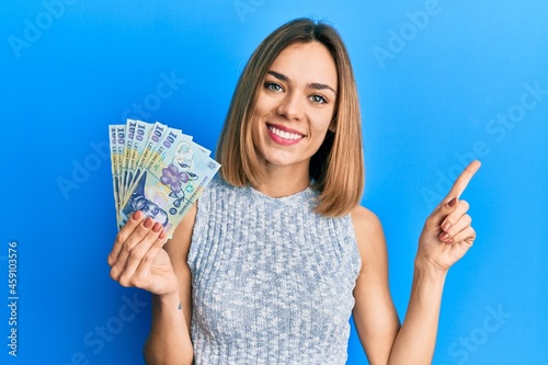 Quadro em tela Young caucasian blonde woman holding 100 romanian leu banknotes smiling happy po