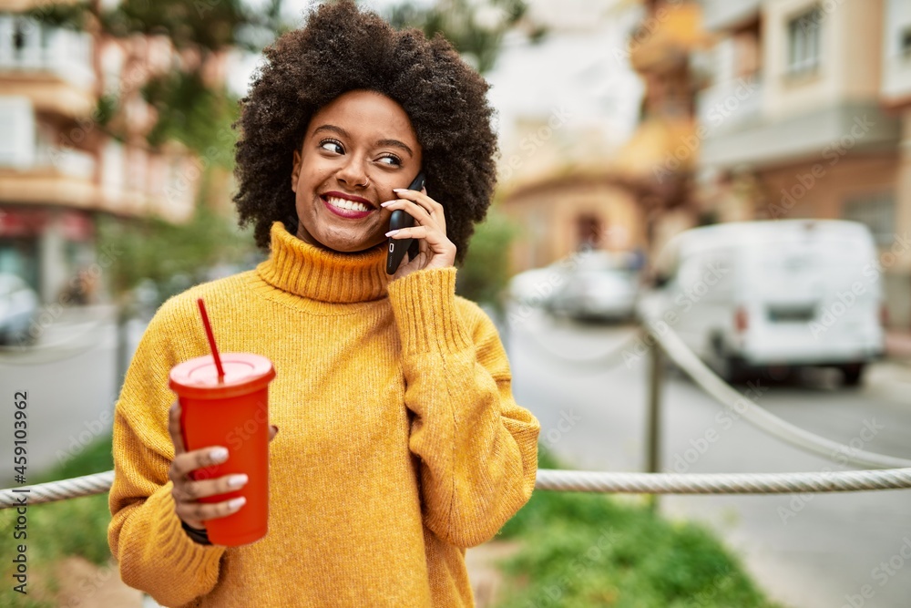 Young african american girl talking on the smartphone and drinking soda at the city. Young african american girl talking on the smartphone and drinking soda at the city.