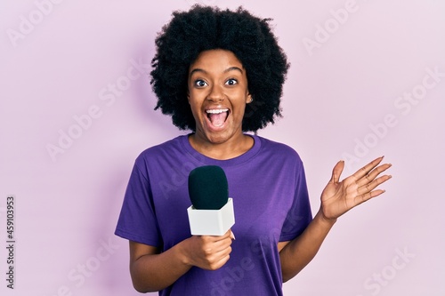 Young african american woman holding reporter microphone celebrating crazy and amazed for success with open eyes screaming excited.