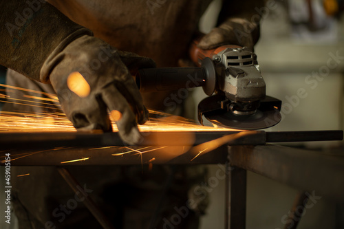Metal processing with a grinder. Sparks from the tool. A man in the workshop wearing gloves with a grinder in his hand.