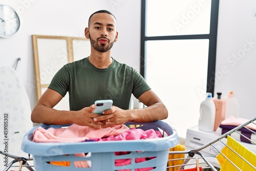 African american man doing laundry using smartphone looking at the camera blowing a kiss being lovely and sexy. love expression.