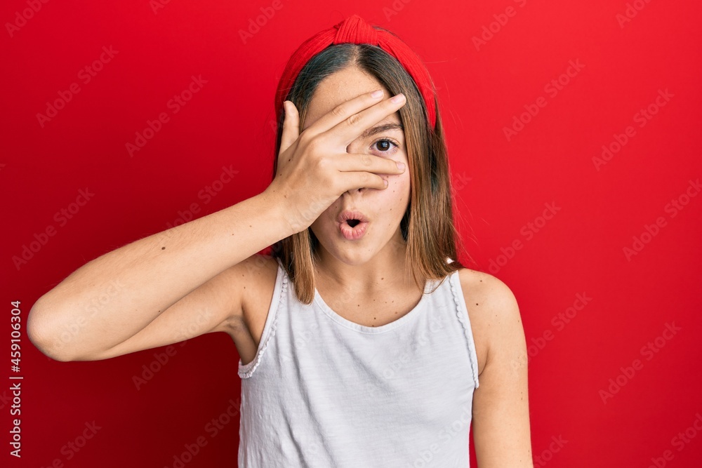 Beautiful brunette little girl wearing casual white t shirt peeking in shock covering face and eyes with hand, looking through fingers afraid Beautiful brunette little girl wearing casual white t shirt peeking in shock covering face and eyes with hand, looking through fingers afraid