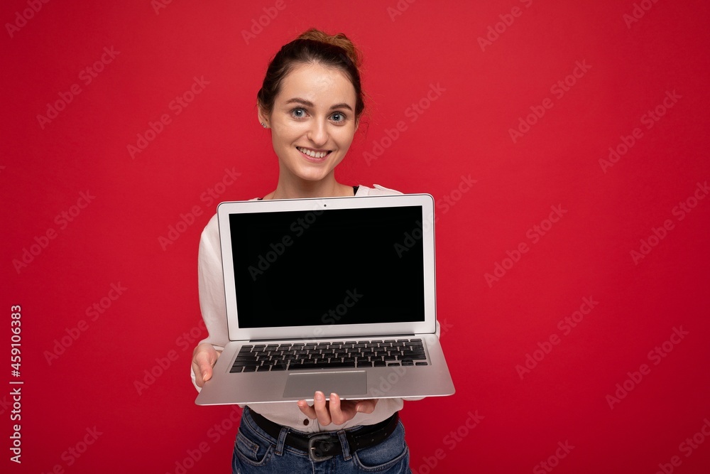 Photo of beautiful young woman holding computer laptop looking at camera isolated over colourful background Photo of beautiful young woman holding computer laptop looking at camera isolated over colourful background