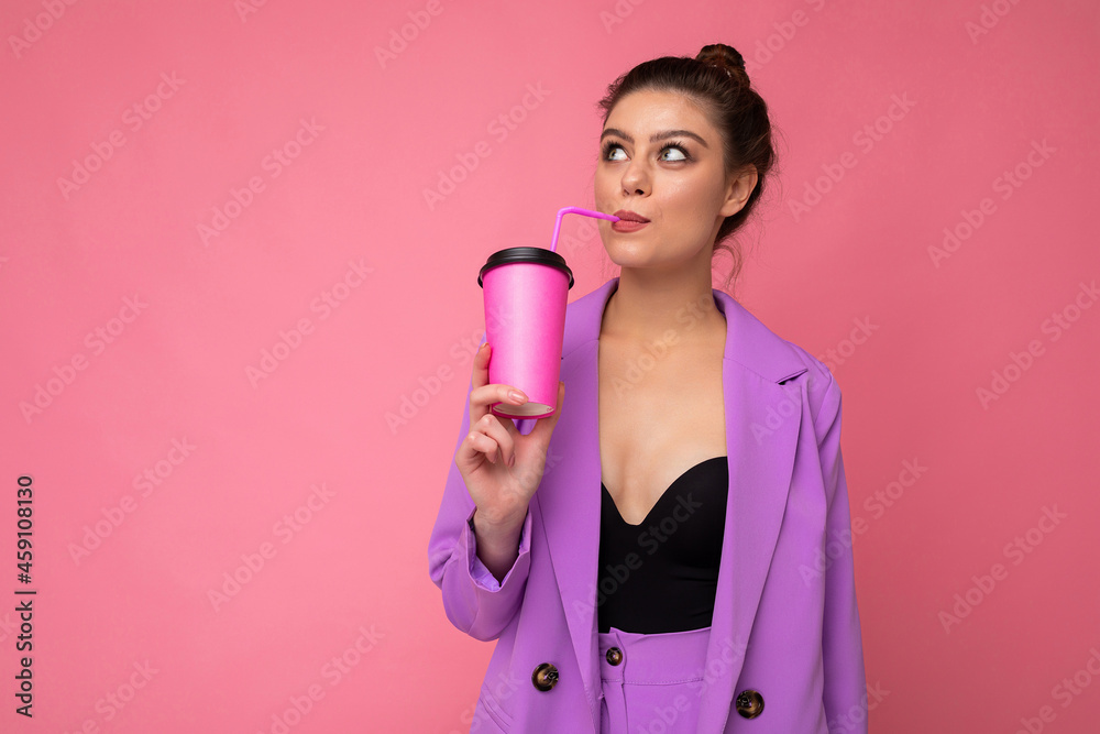Charming young happy thoughtful brunette woman wearing stylish clothes isolated over colourful background wall holding paper cup for mockup drinking milkshake looking to the side and dreaming Charming young happy thoughtful brunette woman wearing stylish clothes isolated over colourful background wall holding paper cup for mockup drinking milkshake looking to the side and dreaming