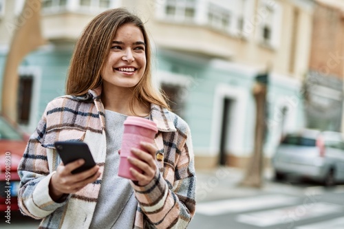 Young blonde woman smiling confident using smartphone holding coffee at street