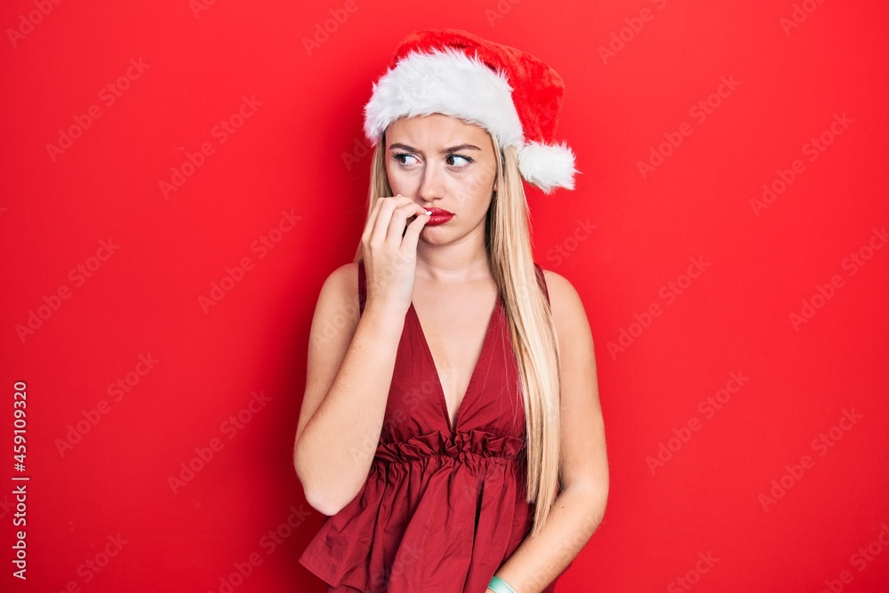 Young blonde girl wearing christmas hat looking stressed and nervous with hands on mouth biting nails. anxiety problem. Young blonde girl wearing christmas hat looking stressed and nervous with hands on mouth biting nails. anxiety problem.