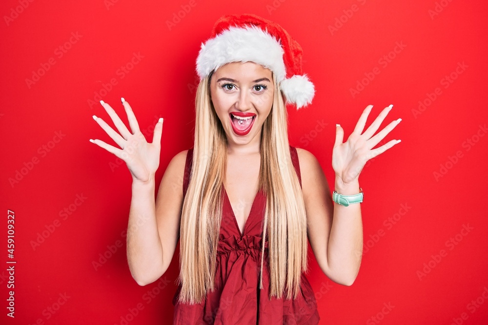 Young blonde girl wearing christmas hat celebrating crazy and amazed for success with arms raised and open eyes screaming excited. winner concept Young blonde girl wearing christmas hat celebrating crazy and amazed for success with arms raised and open eyes screaming excited. winner concept