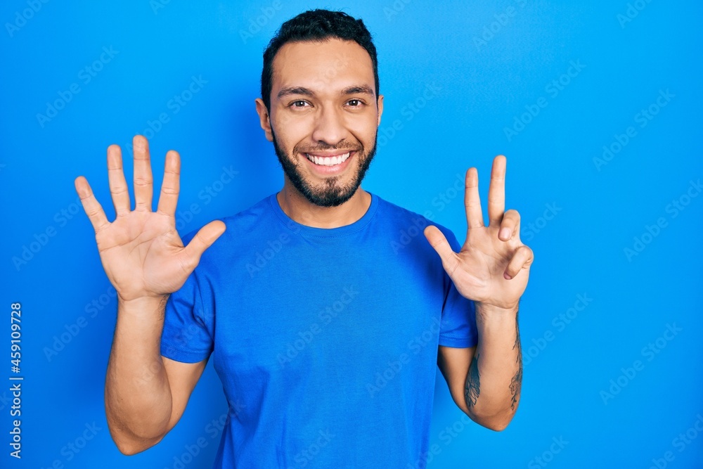 Naklejka premium Hispanic man with beard wearing casual blue t shirt showing and pointing up with fingers number eight while smiling confident and happy.